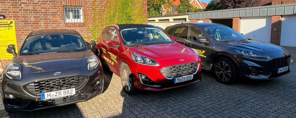 Drei Ford-Fahrschulwagen in Grau, Rot und Schwarz nebeneinander