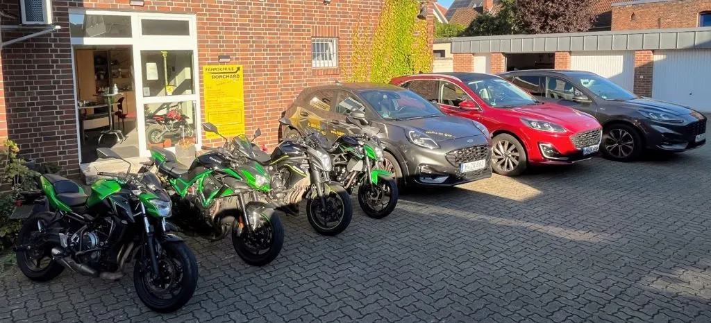 Fuhrpark der Fahrschule Borchard: vier Motorräder und drei Ford-Fahrschulautos vor der Fahrschule