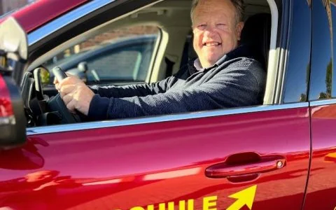 Fahrlehrer Mathias am Steuer eines roten Fahrschulautos